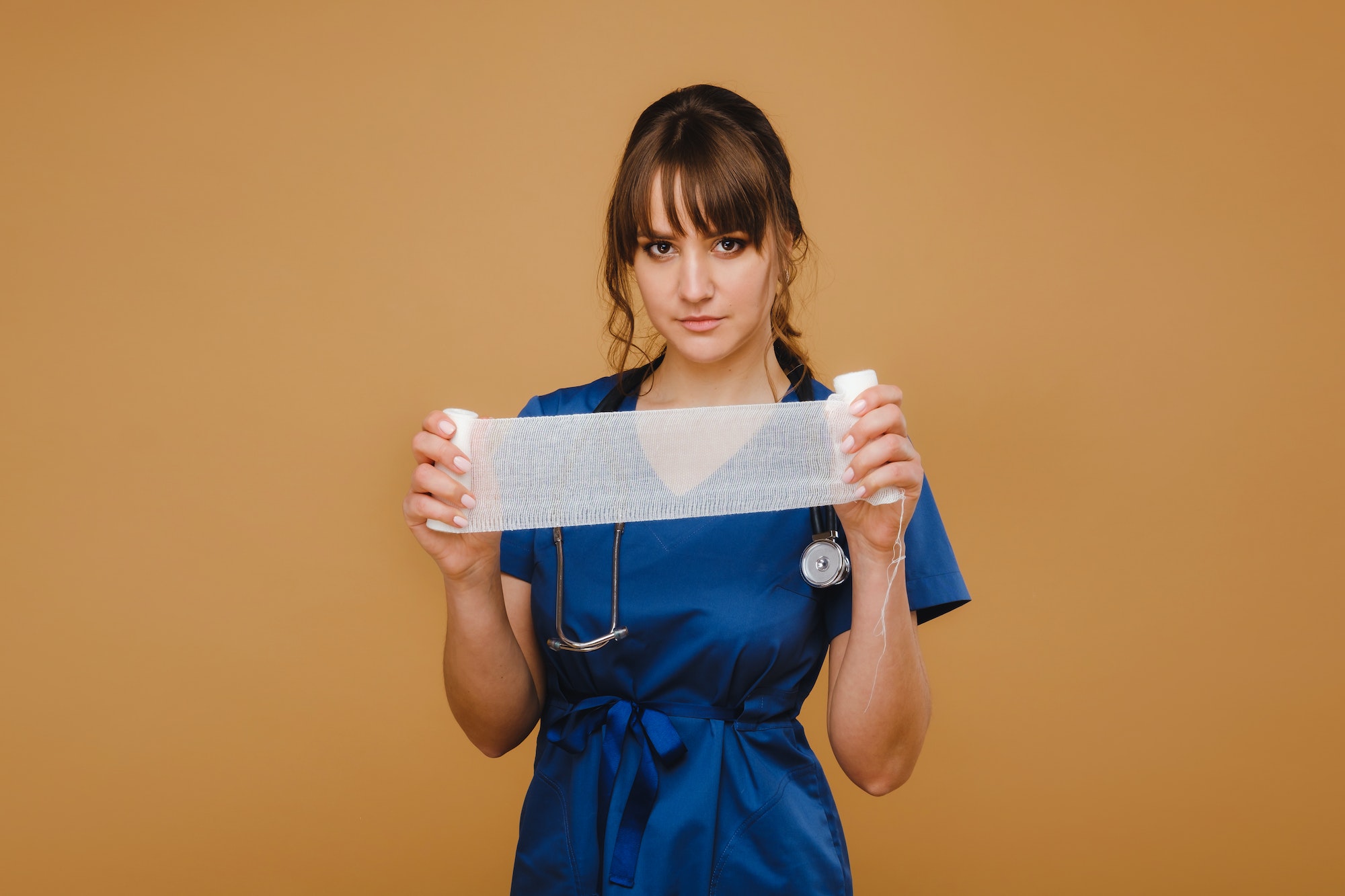 medic woman in white coat and mask holds a twisted gauze bandage for dressing wounds, white
