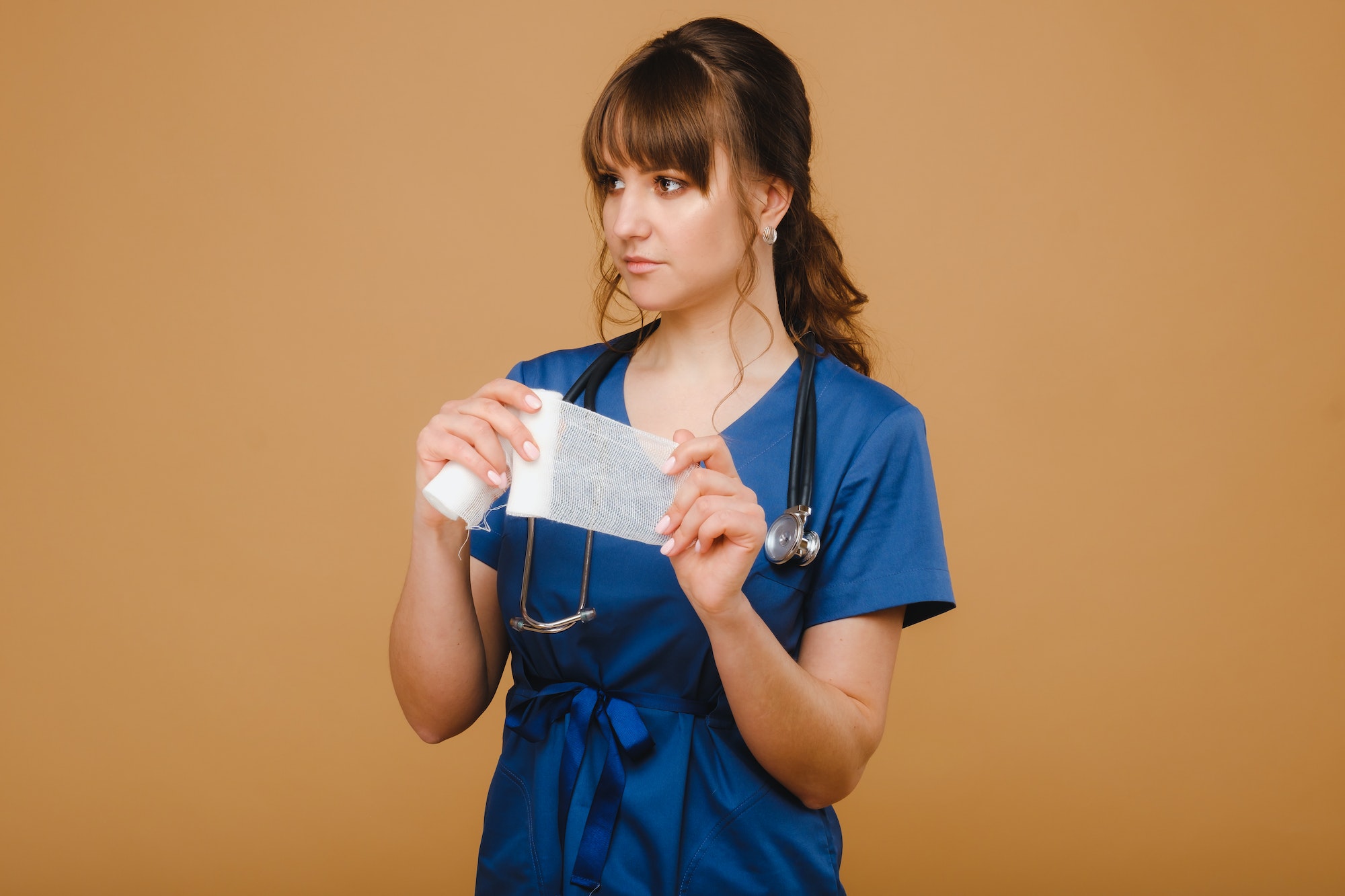 medic woman in white coat and mask holds a twisted gauze bandage for dressing wounds, white